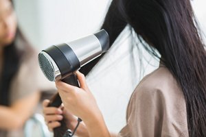 Brunette woman drying her hair in front of a mirror